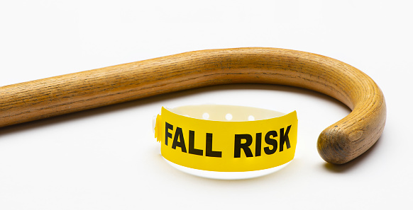 A yellow, Fall Risk medical bracelet on white background with wooden cane