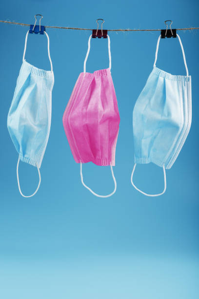istock Three medical masks hanging on a rope, pink and blue on a blue background. 1394828251