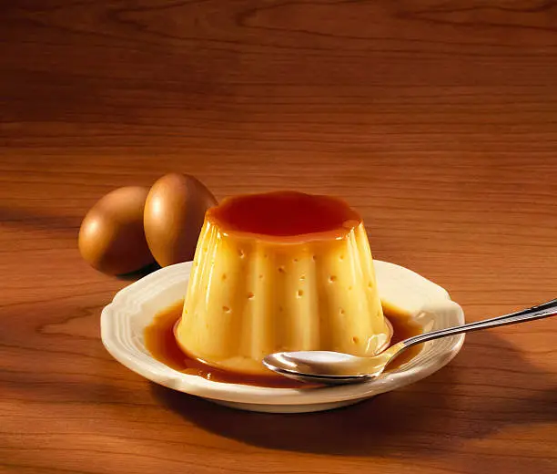 Creme caramel dessert with eggs and spoon on a wood table, with copyspace