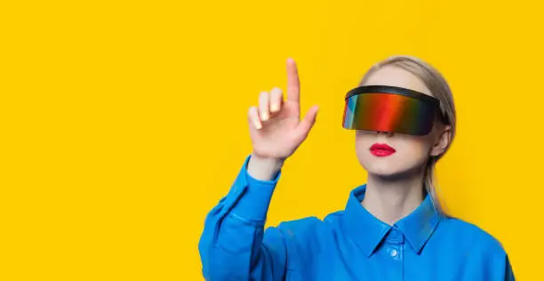 Photo of Stylish woman in blue shirt and VR glasses on yellow background