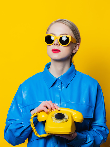 Teenage girl in love speaking with her boyfriend on the phone, isolated on blue wall background