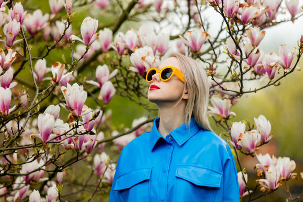 piękna blondynka w okularach przeciwsłonecznych i niebieskiej koszuli obok drzewa magnolia na wiosnę - sweet magnolia tree blossom white zdjęcia i obrazy z banku zdjęć