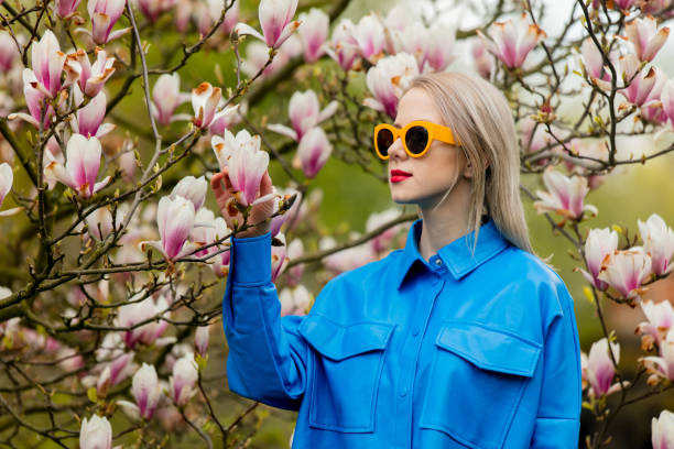 piękna blondynka w okularach przeciwsłonecznych i niebieskiej koszuli obok drzewa magnolia na wiosnę - sweet magnolia tree blossom white zdjęcia i obrazy z banku zdjęć