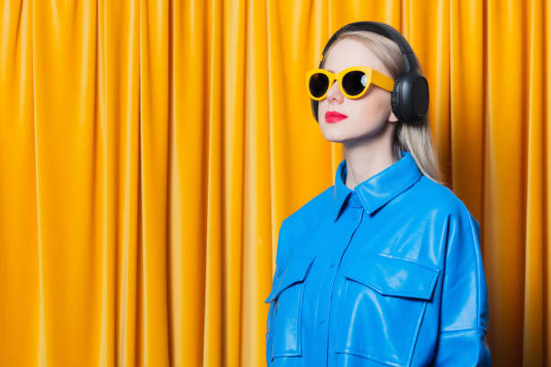 woman in blue shirt and yellow sunglasses with music headphones stock photo