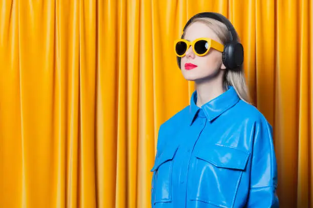 Photo of woman in blue shirt and yellow sunglasses with music headphones