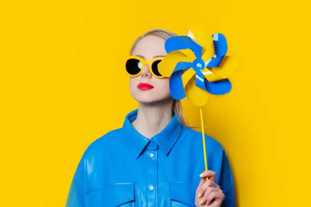 Photo of Stylish ukrainian woman with pinwheel in urkaine flag colors on yellow background