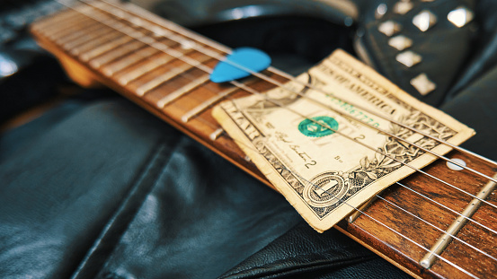 One dollar bill, guitar neck, plectrum and leather jacket close-up