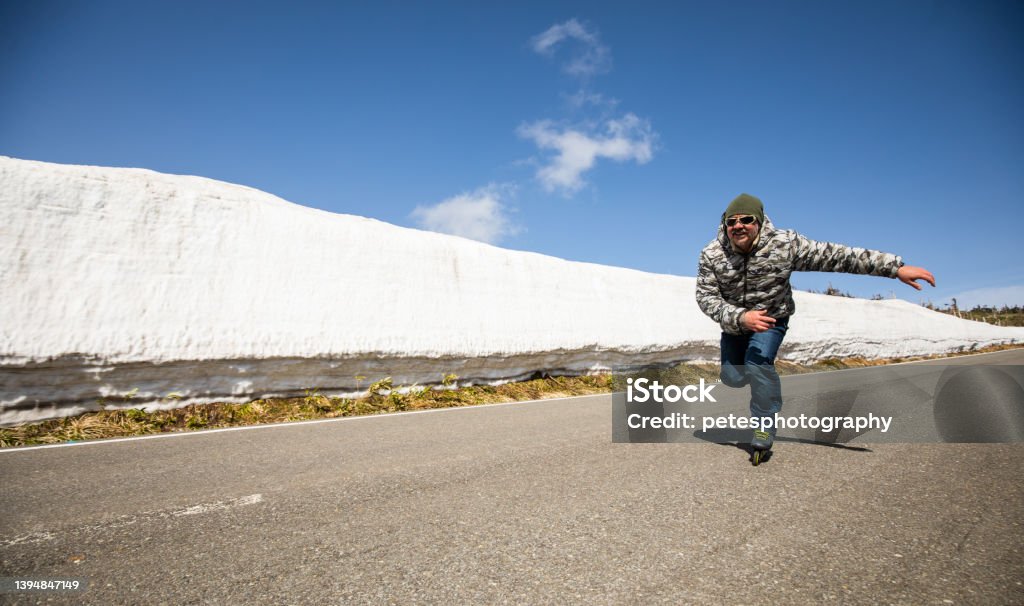 An Inline Skater skates along a mountain road lined with snow walls Man inline skating past low angle camera along a snowy mountain road with snow walls on the side of the road. 40-44 Years Stock Photo