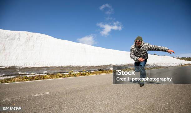 An Inline Skater Skates Along A Mountain Road Lined With Snow Walls Stock Photo - Download Image Now