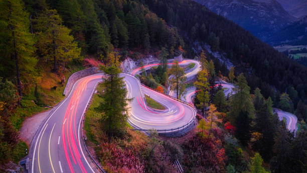 Maloja pass, Switzerland. A road with many curves among the forest. A blur of car lights. Landscape in evening time. Maloja pass, Switzerland. A road with many curves among the forest. A blur of car lights. Landscape in evening time. maloja region stock pictures, royalty-free photos & images