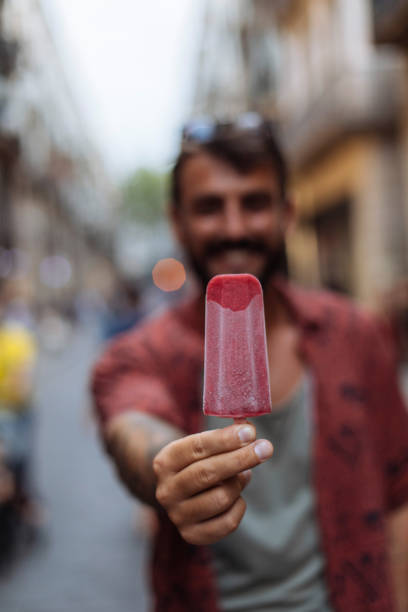 Smiling young man eating ice cream while walking through a city street