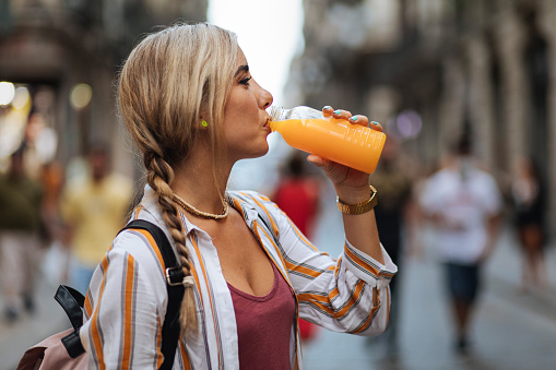 Young blond drinking fresh juice while standing in a city street