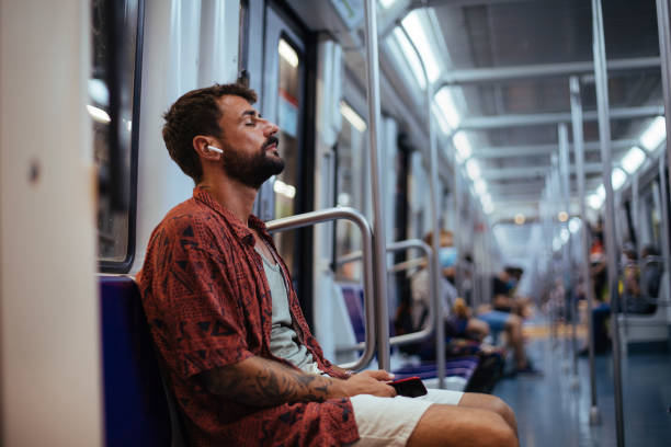 Taking a break while in transit Young man listening to music on his headphones and resting while sitting on a subway train tired after work stock pictures, royalty-free photos & images