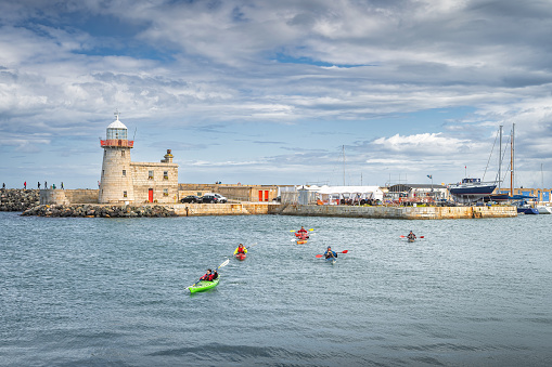 Dublin, Ireland, Aug 2019 Group of people kayaking in Howth marina with Howth Lighthouse in the background