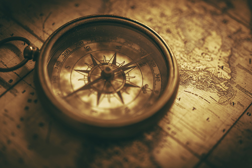 Classic Vintage Compass Device on a Aged Map. Sepia Colour Grading Journey and Adventure Theme.