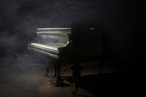 Old grand piano on a smoky stage lit by a single spotlight