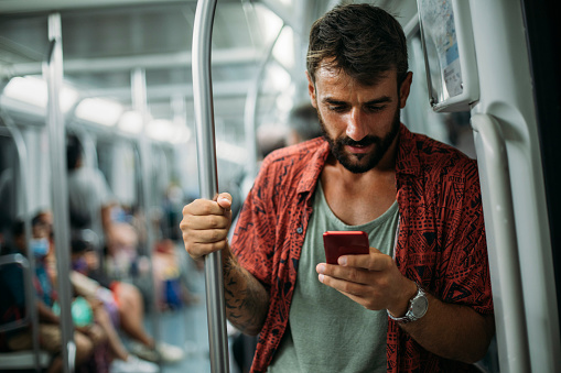 Young man using his phone while standing in a subway train