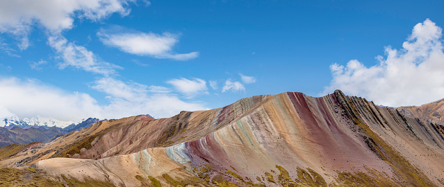 Palcoyo Rainbow Mountain, Cusco, Peru - April 28, 2022; In Palcoyo there are three Rainbow Mountains. The Rainbow Mountains are composed of stratified layers of sandstone. These fine-grained rock layers contain large amounts of iron and other minerals, which give the mountains the pigments for the various colored stripes\n\nFrom Palcoyo it's possible to see the glacial Ausangate Peak. Palcoyo is also famous for its stone forest area which is 4900 metres above sea level. The name is given due to the look of the big standing sharp stones that gives the illusion of a forest.
