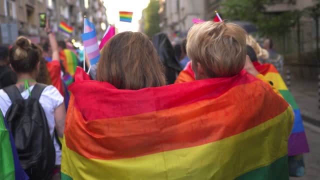 Zwei Frauen, die an einer Gay-Pride-Feier teilnehmen, dicht gedrängt unter einer Regenbogenflagge