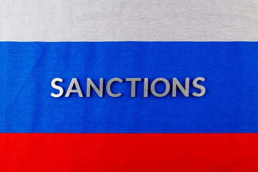 the word sanctions laid with silver metal letters on russian tricolor flag in directly above perspective