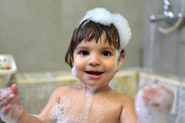 Cute little girl enjoys a bath while her mother sits next to her