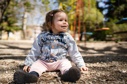 One baby small caucasian child little girl in park sitting on the ground in bright spring day real people childhood development learning and family concept copy space happy smile
