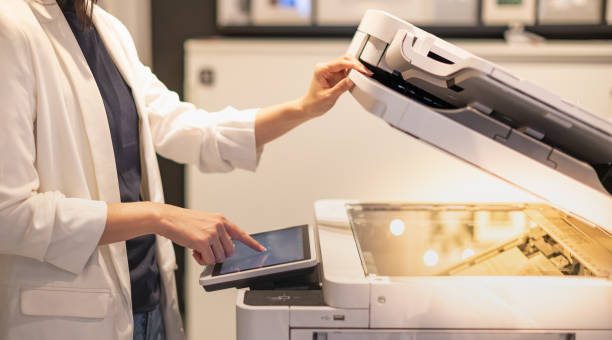 Female standing and hand pressing button on a copy machine in the office. stock photo