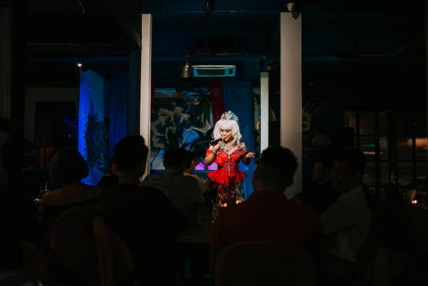 Asian drag queen in spot lit stage performance at pub with audience in silhouette
