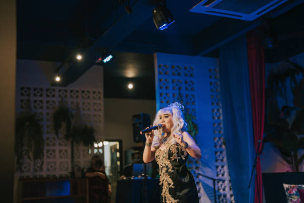 istock Asian drag queen in spot lit stage performance at pub with audience in silhouette 1394869202