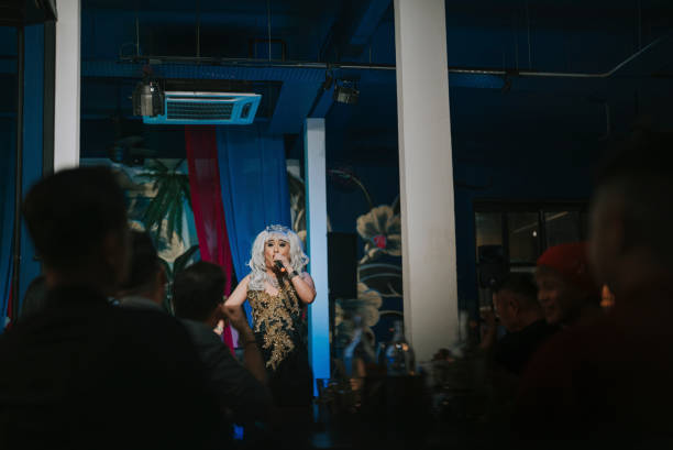 drag queen asiática en una actuación en el escenario iluminado en un pub con el público en silueta - spot lit fotografías e imágenes de stock