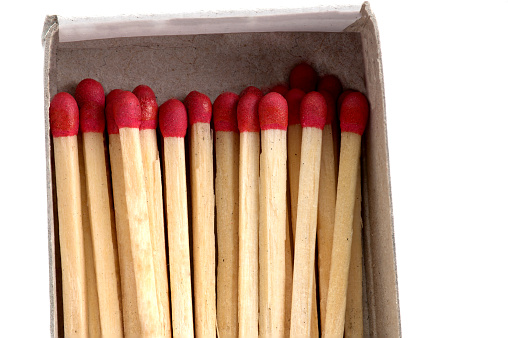 extreme close up of stacked matches with red match heads in open cardboard matchbox on white background