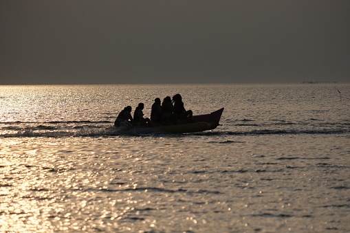 A group of excited tourist is riding a banana boat over brightly lit sea
