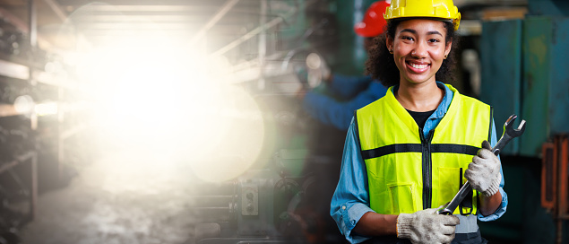 Black Woman engineer wearing safety hardhat helmet and large wrench working at old factory. Metal lathe industrial manufacturing factory