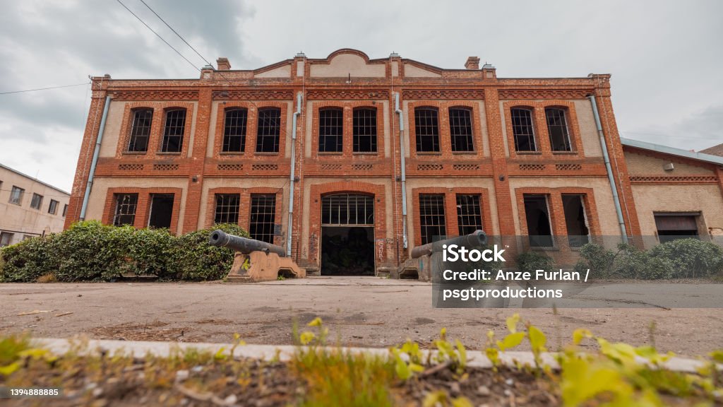 Old industrial warehouse in Kragujevac, Serbia, made of red bricks. Ruined windows and deserted interior on a cloudy day with cannons on the entrance. Abandoned Stock Photo