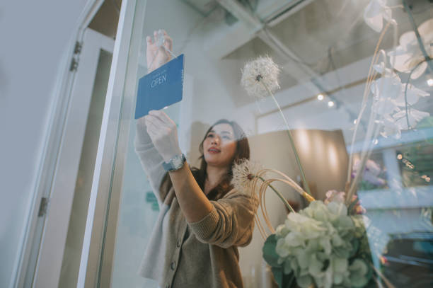 azjatycka chinka właścicielka kwiaciarni ponowne otwarcie dla firmy obracając znak na szklanym oknie przed jej kwiaciarnią - owner florist sign business zdjęcia i obrazy z banku zdjęć