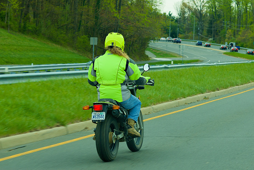 Fairfax, Virginia, USA - April 21, 2022: A motorbike rider wearing a neon yellow helmet and jacket travels on Route 123 through the City of Fairfax.