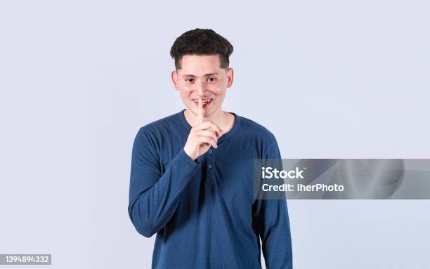 Man Gesturing Keep Quiet Guy Smiling With Finger On Mouth Showing Hush Gesture Attractive Male Whispering Silence Stock Photo - Download Image Now