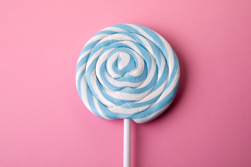 Blue lollipop on a pink background. Sweets, party and unhealthy food.