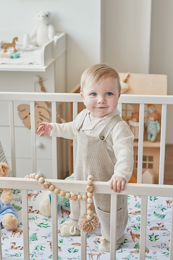 Wonderful baby boy with blue eyes in crib. Child playing with toys in nursery. Early development, kindergarten, nursery, playroom. Children's Day, Mother's Day.