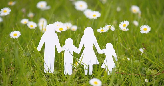 Family paper cut out is standing in a meadow, parents with daughter and son, environment concept, spring and summer season