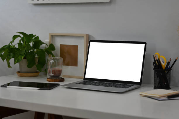 istock White modern office table with laptop with blank white screen, tablet, coffee cup and note books with no people, for business and technology concept. 1394904676