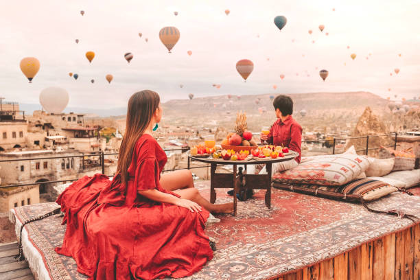 カップル カッパドキアでの旅行 渓谷の上空を飛ぶカラフルな熱気球 トルコの特別な朝食旅行先で日の出時間 - ロックフードゥー ストックフォトと画像