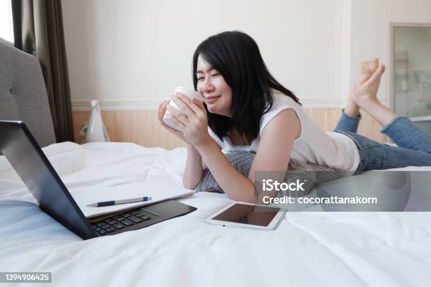 Smiling Asian Businesswoman Is Laying For Drink A Cup Of Coffee And Working With Laptop In Bedroom On Holiday She Is Online Working From Home With Technology During The Covod19 Outbreak Concept Stock Photo - Download Image Now