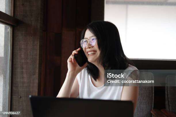 Smiling Young Asian Woman Is Wearing Glass And Calling With Smartphone And Online Working With Laptop In Living Room Work From Home For Covod19 Outbreak Concept Stock Photo - Download Image Now