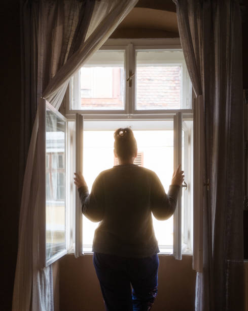 vista trasera de la mujer mirando a la calle desde la ventana del dormitorio - violence domestic violence women domestic life fotografías e imágenes de stock