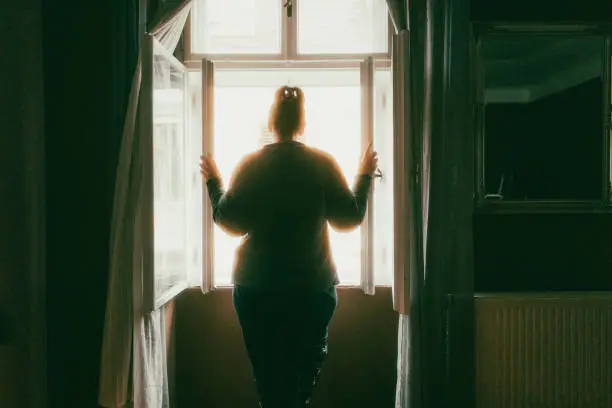 Photo of Rear view of woman looking at street from bedroom window