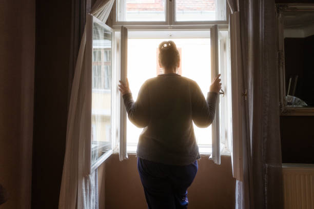 vista trasera de la mujer mirando a la calle desde la ventana del dormitorio - violence domestic violence women domestic life fotografías e imágenes de stock