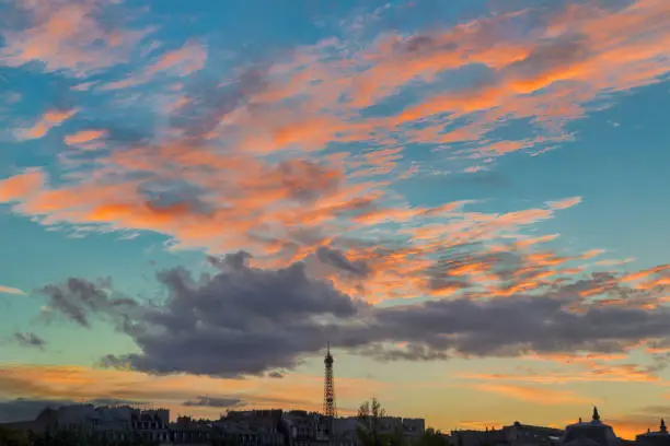 The Eiffel Tower in front of salmon-colored clouds at sunset seen from the Right Bank of the River Seine.