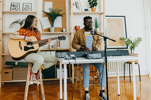Young Caucasian woman and African American man playing synthesiser and guitar