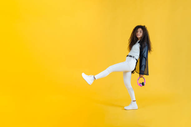 Young woman taking long step while walking in studio shot with yellow background stock photo
